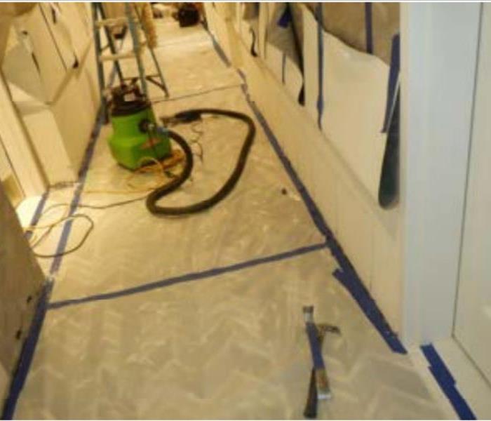 Commercial-grade fans drying out carpet and walls in a hotel hallway.