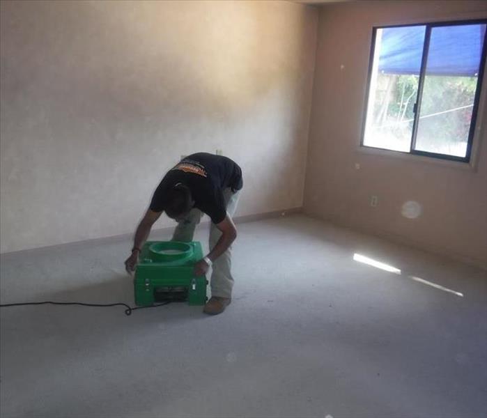 A water damage technician placing an air scrubber down in a room.